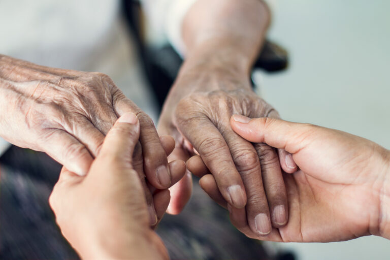 Hands of young caregiver holding the hands of an elderly patient.