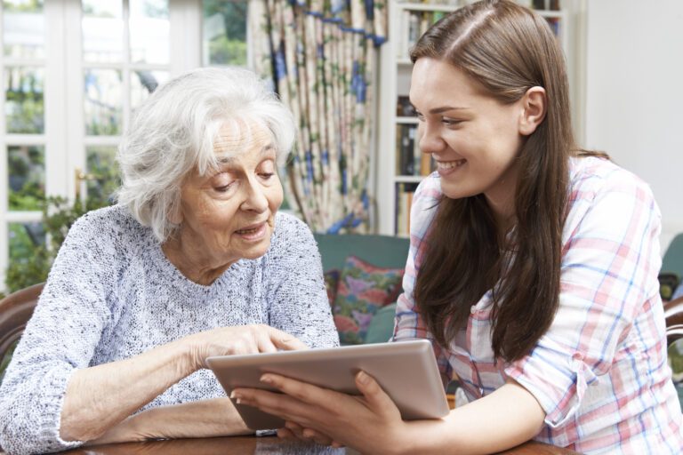 A caseworker assisting an older adult with a digital tablet at home, illustrating person-centered aging services and technology-enabled care coordination.