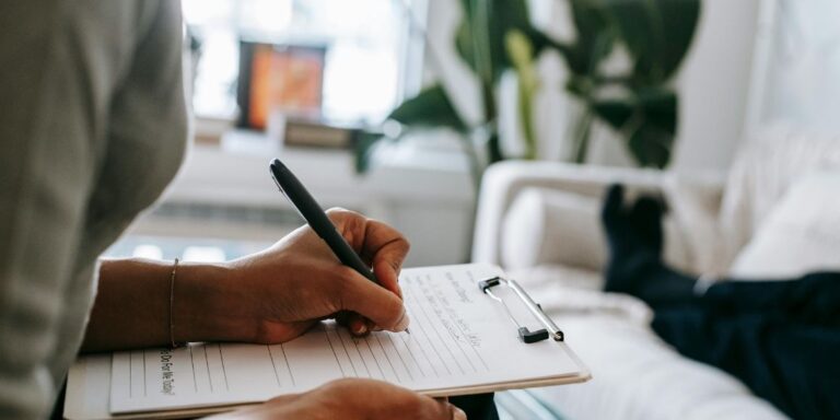 Therapist taking notes manually as her patient lies down, highlighting the lack of mental health case management software.